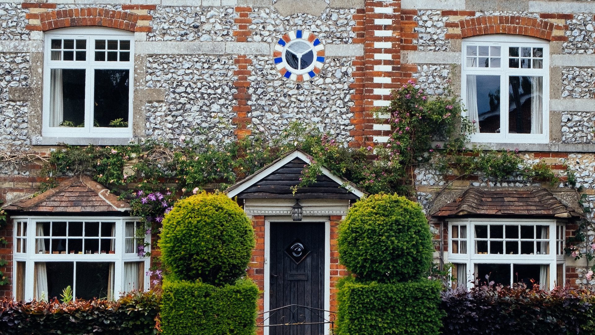 A large frontage to a rural UK home, with styled hedges forming a walkway to a front door.