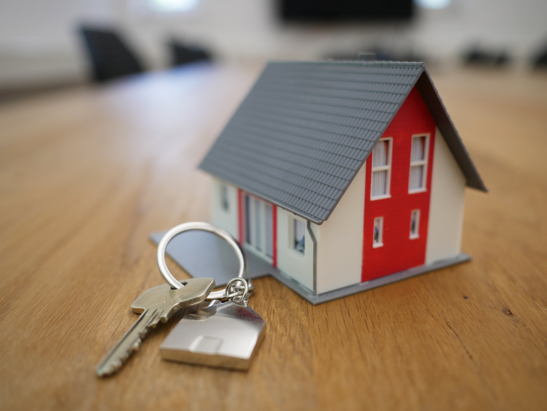 A set of house keys sat next to a similar sized miniature house model, on top of a wooden table.