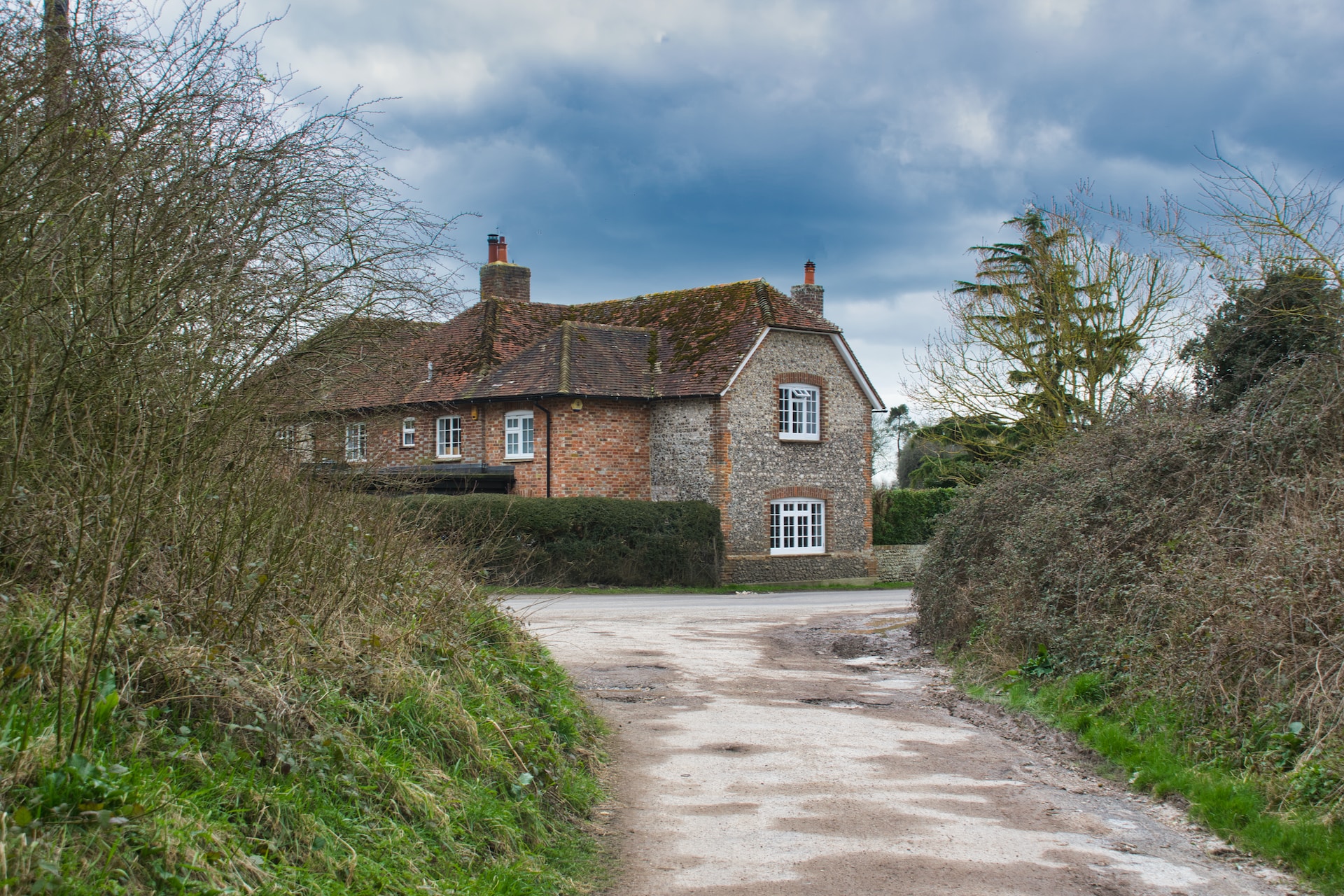 A large detached home viewed from the bottom of a long driveway in the UK countryside.