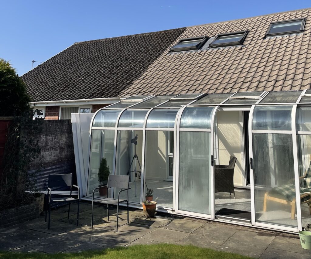 The conservatory of a bungalow, viewed from the garden under bright sunlight.